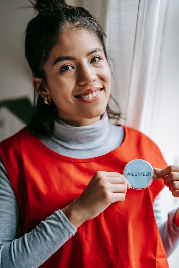 approach-img Confident female volunteer smiling while holding a volunteer badge indoors.