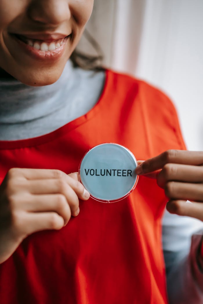 impact-img Close-up of a smiling volunteer holding a badge in a bright setting.